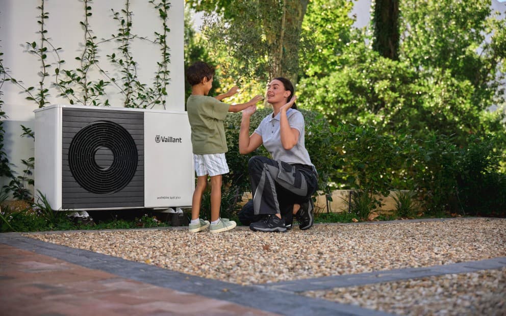 Installateur dans le jardin avec un enfant devant une PAC Vaillant